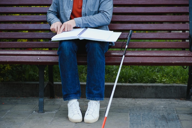 Blind man reading braille book sitting on bench in summer park resting