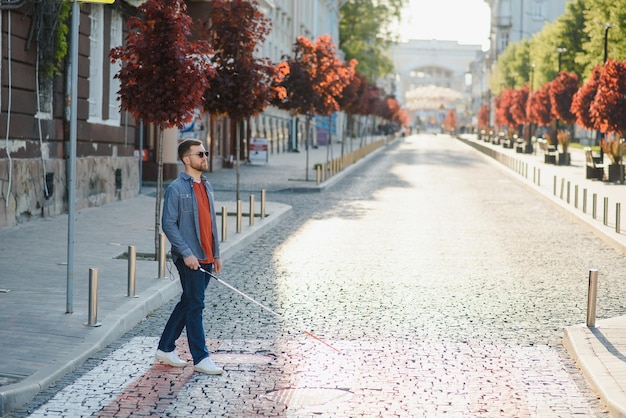 Blind person with white cane crossing street in city closeup