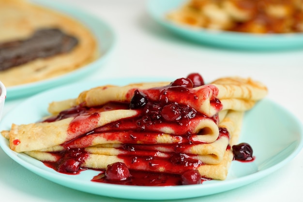 Blini pancakes with red berry jam close-up on a blue plate on a light background