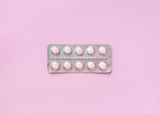 A blister of soft pink pills in the middle on pink background. Monochrome simple flat lay with pastel texture. Medical concept. 