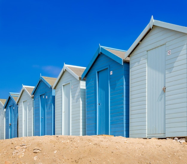 Block of blue and white beach huts on the beach under a blue sky and sunlight