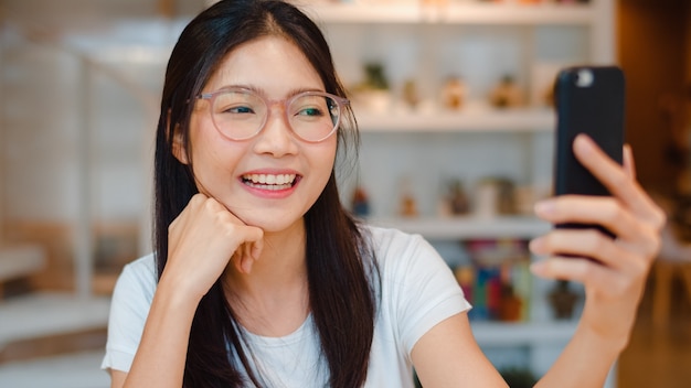 Blogger Asian friendly women influencer waving hand making video call at night cafe