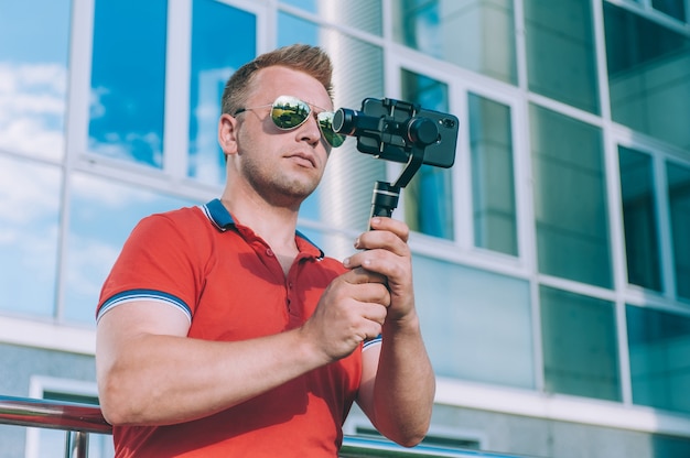 Blogger in the city shoots video on a smartphone with a manual camera stabilizer.