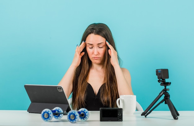 Blogger girl is closing eyes by holding hands on tempels on blue background