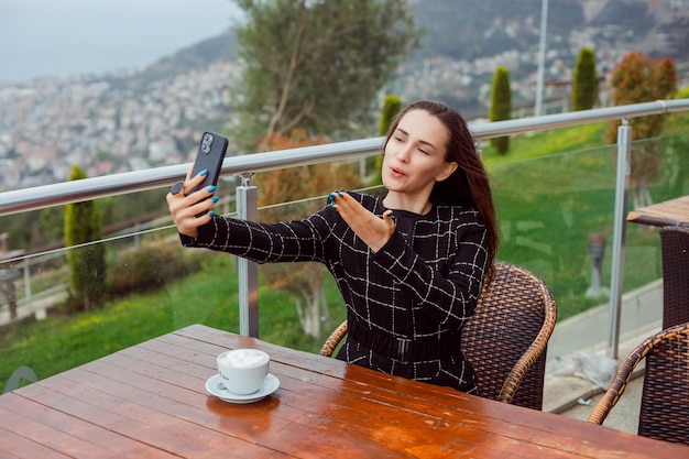 Blogger girl is taking selfie with her smartphone by blowing kiss by sitting on city view background