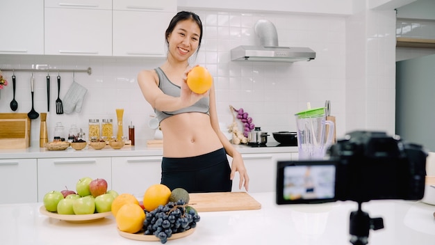 Blogger sporty Asian woman using camera recording how to make orange juice video for her subscriber