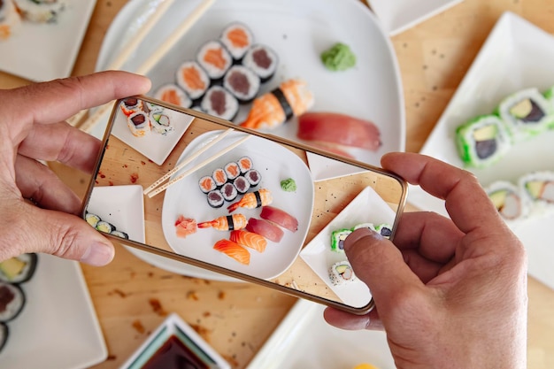 Blogger with mobile phone taking photo of delicious sushi on table top view