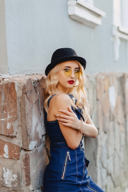 Blond attractive girl in sunglasses and stylish hat at summer sunshine urban