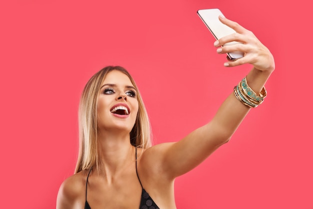 Blond beautiful adult woman posing over pink with smartphone