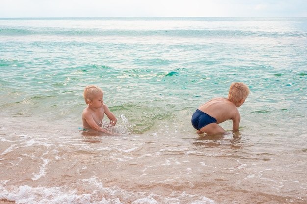 Blond boy brothers playing in the sea water on a sandy beach on a summer day Fun vacation