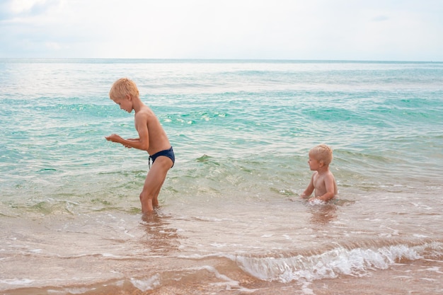 Blond boy brothers playing in the sea water on a sandy beach on a summer day Fun vacation