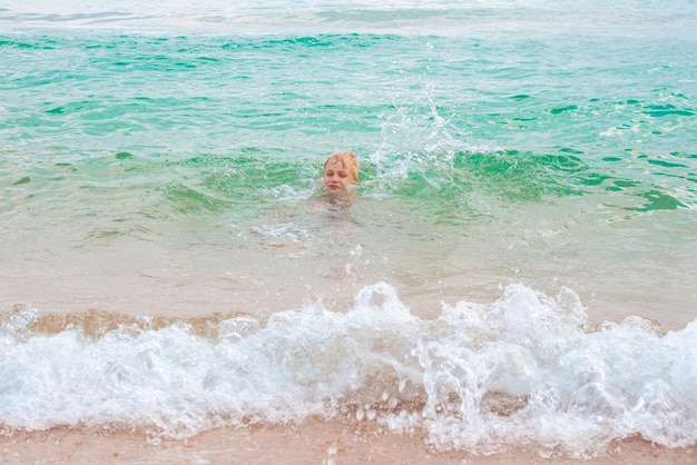 A blond boy learns to swim in the seawater on a summer day at the coast Fun vacation