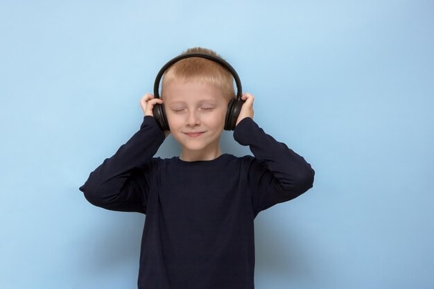 Blond boy listens to music in headphones with closed eyes on a blue background