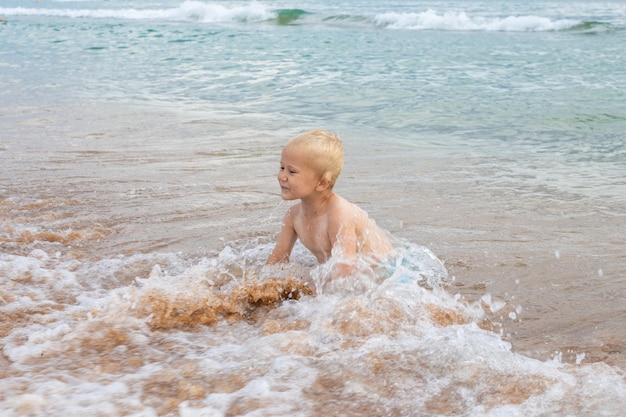 A blond boy plays in the sea wave on a sandy beach Fun summer vacation