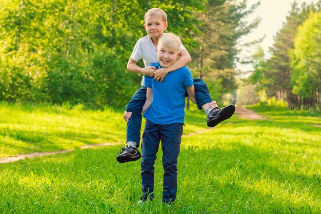 Blond boy riding on the back of a friend in the green park