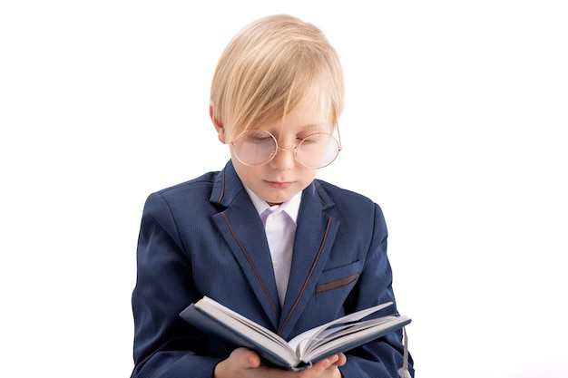 Blond boy in school uniform reads textbook Schoolboy with big glasses looks at book Isolated on white background