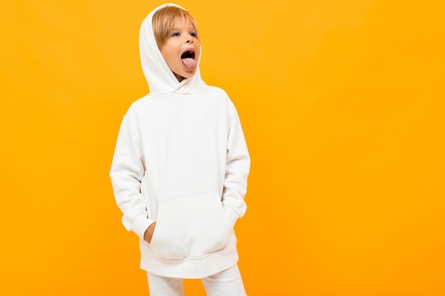 blond boy in a white sweater is grimacing on orange