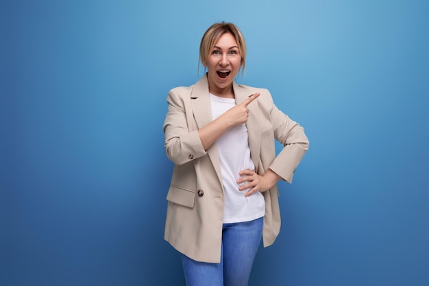 Blond business woman in a beige jacket shows for having an idea with a finger on a studio background