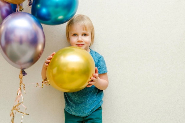 Blond cute happy Child kid boy celebrating third birthday with colorful balloons at partyhome in front of wallbaby smiling looking at cameraadorable caucasian babyFestive background decoration