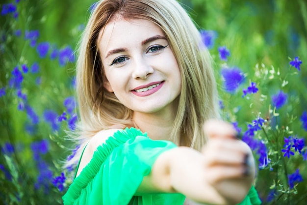 Blond european girl in a green dress  on nature with blue flowers