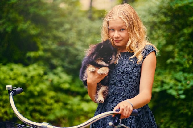 Blond girl on a bicycle holds a Spitz dog.