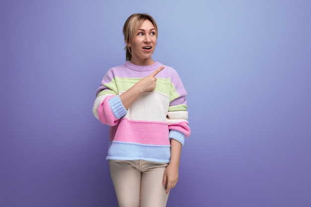 Blond girl in surprise shows her hand to the side on a purple background with copy space