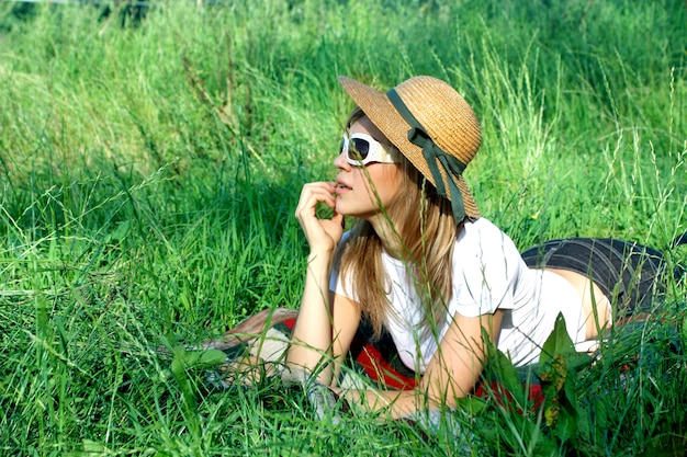 Blond girl with hat and sunglasses laying on grass field