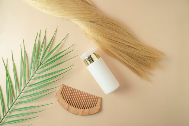 Blond hair and a hair serum and comb for extention lying on a beige background