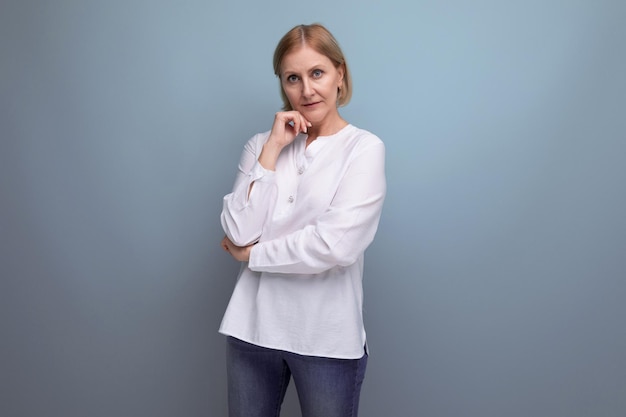 Blond hair woman of mature years in a white shirt smiling on a studio background