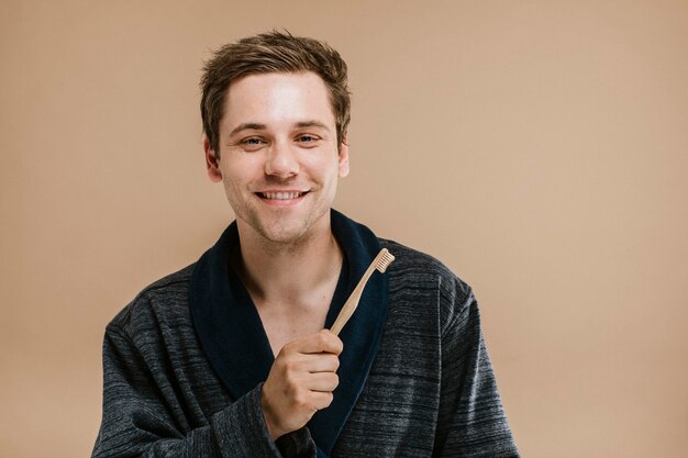 Blond man in a dark robe holding a wooden toothbrush