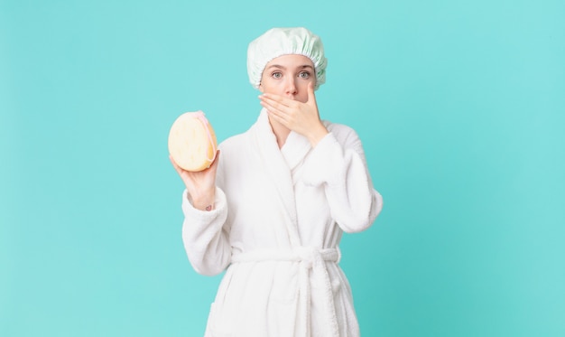 Blond pretty woman covering mouth with hands with a shocked and wearing bathrobe