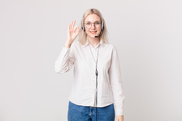 Blond pretty woman feeling happy, showing approval with okay gesture telemarketing concept