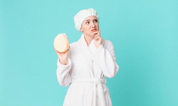 Blond pretty woman thinking, feeling doubtful and confused and wearing bathrobe