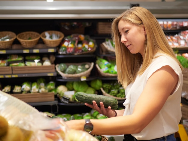 Blond woman buy cucumber at supermarket