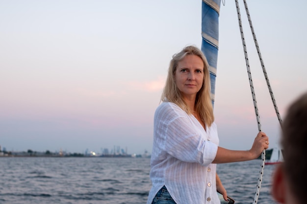 Photo blond woman on a sailboat at dusk with a distant city skyline a scene of contemplation and escape copy space