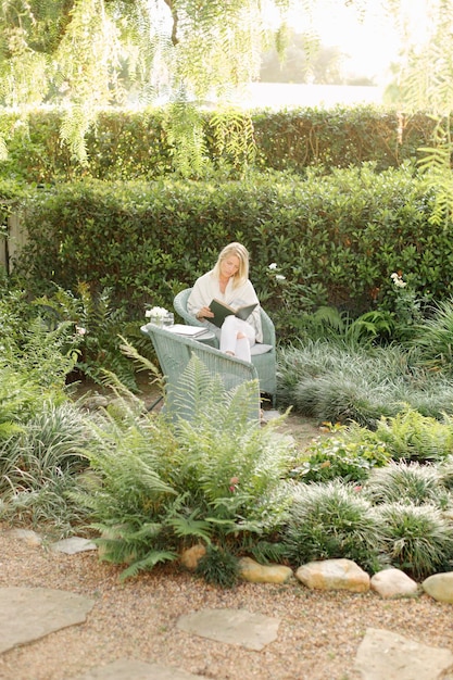 Photo blond woman sitting in a wicker chair in a garden reading