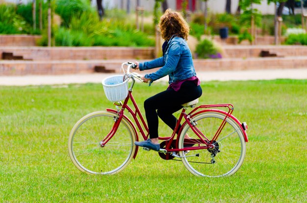 Blond woman walking in the park with a blue denim on a red bicycle