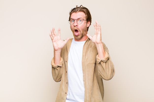 Blonde adult caucasic man screaming with hands up in the air, feeling furious, frustrated, stressed and upset