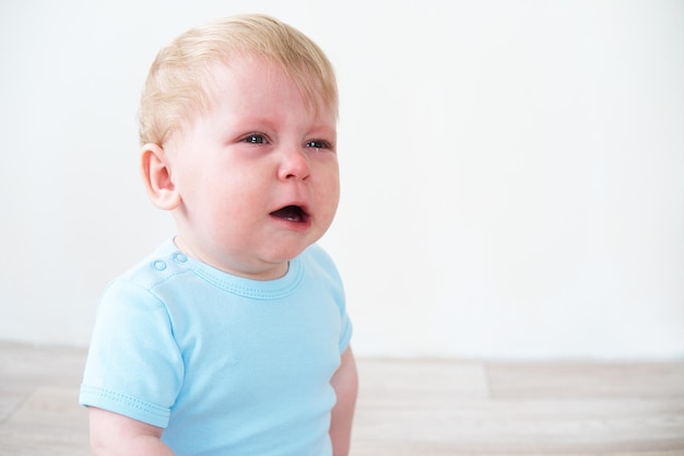 blonde baby in blue shirt crying sitting on floor at home