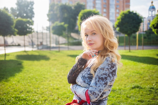 Blonde in a blue dress posing near the buildings in a city park