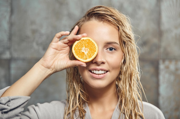 Blonde caucasian female model with a piece of orange near her face close up shot in the bathroom