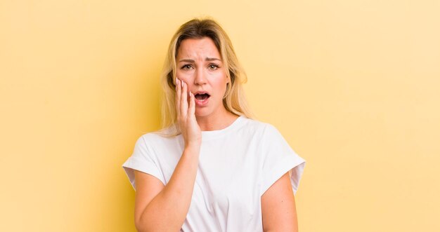 Photo blonde caucasian woman openmouthed in shock and disbelief with hand on cheek and arm crossed feeling stupefied and amazed