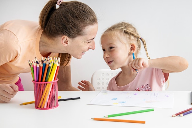 Blonde child girl draws with colored pencils sitting at the table Top view flat lay