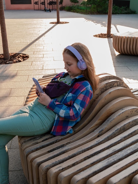 Blonde child in headphones listening to music podcast smartphone outside Young girl learn online lesson enjoy audio book