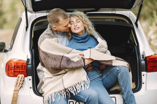 Blonde curly woman and man sitting in a trunk in car in autumn forest with a guitar