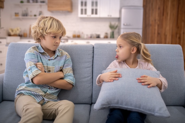 Blonde cute girl with a pillow showing tongue to her brother