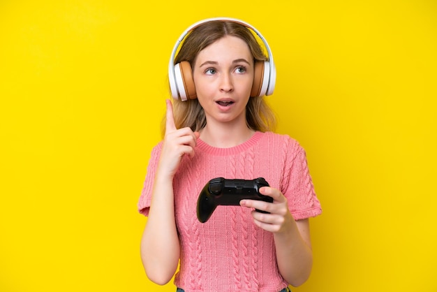 Blonde English young girl playing with a video game controller isolated on yellow background