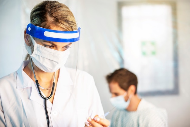 Blonde female doctor with protective mask ready to do the sting for virus flu. Patient background
