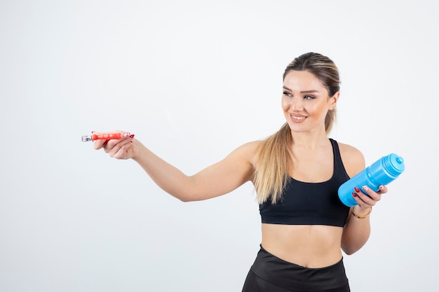 Blonde fit woman in black top standing and holding bottle of water with expander.  