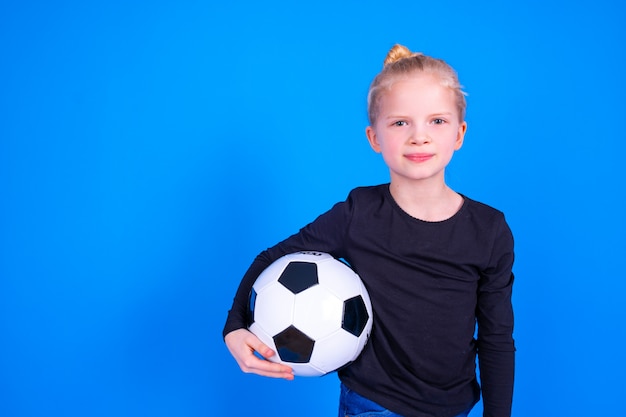 blonde girl in black shirt holding soccer ball in hands over blue